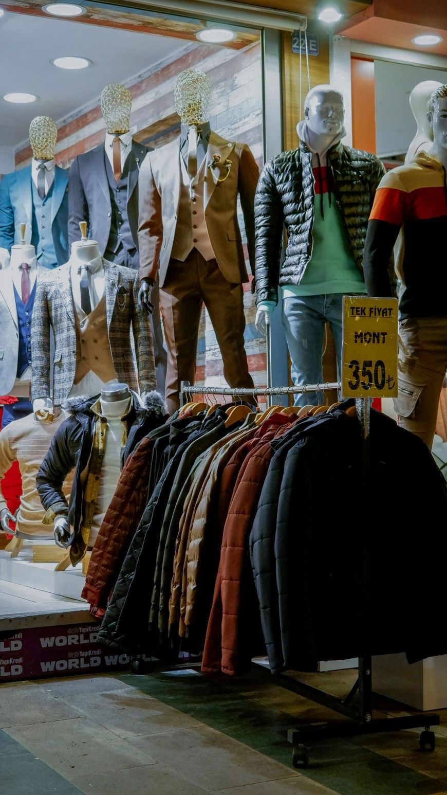 Clothing store display with mannequins wearing sweaters and jackets, plus racks of hanging clothes and a sale sign.