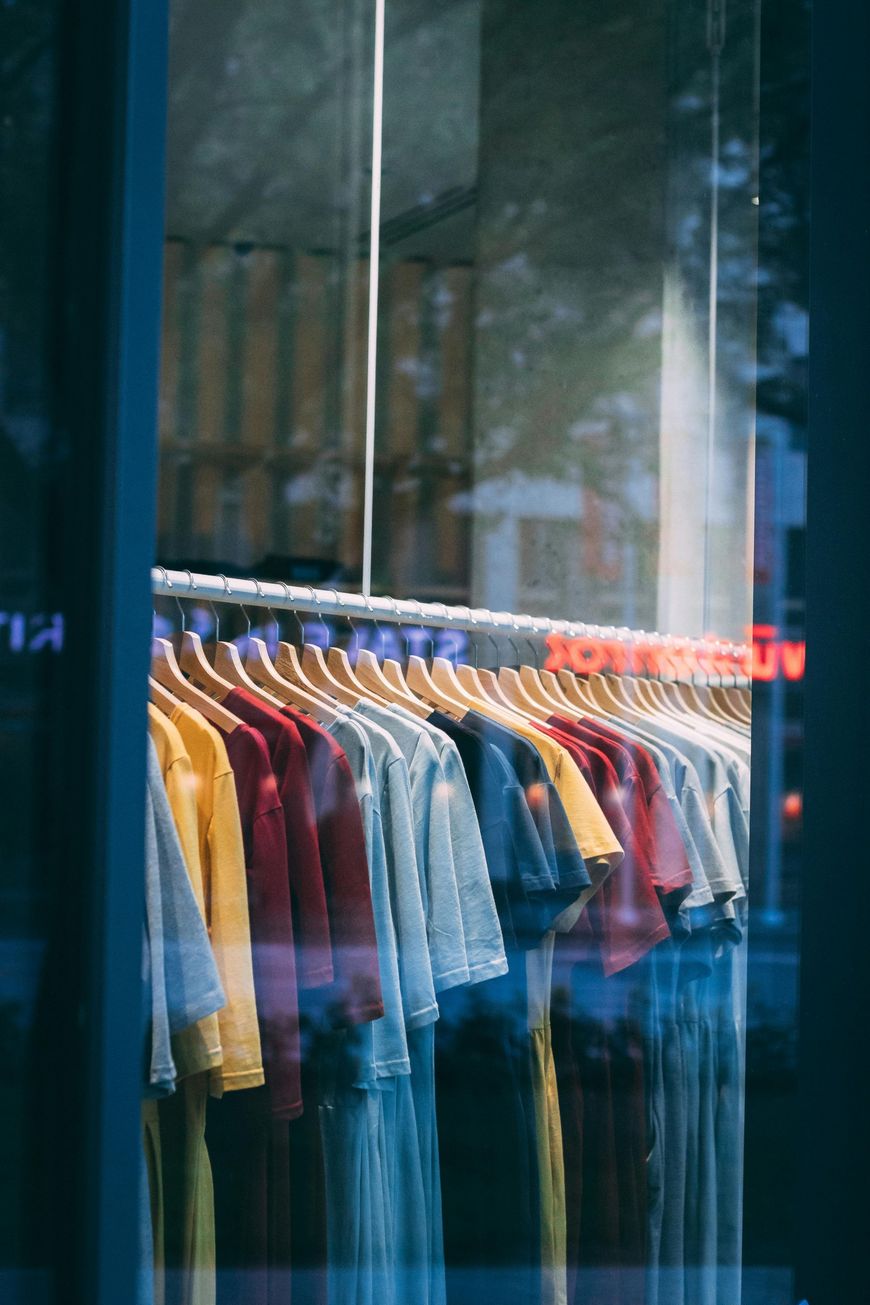 Clothing store window with a row of colorful shirts on hangers behind glass