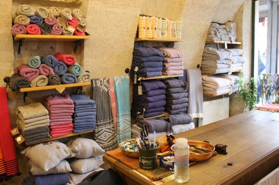 Shelves of folded fabrics and towels in a cozy textile shop, with a wooden counter in front