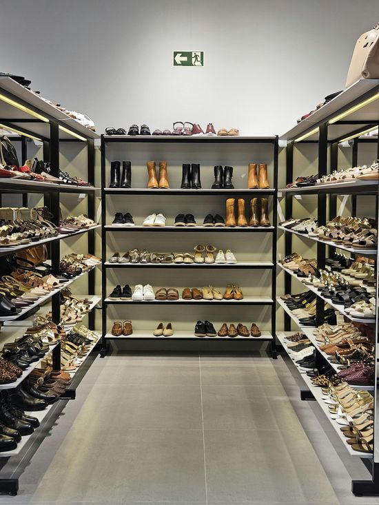 Shoe store aisle with shelves of shoes lining both sides and the back wall in a bright, narrow room