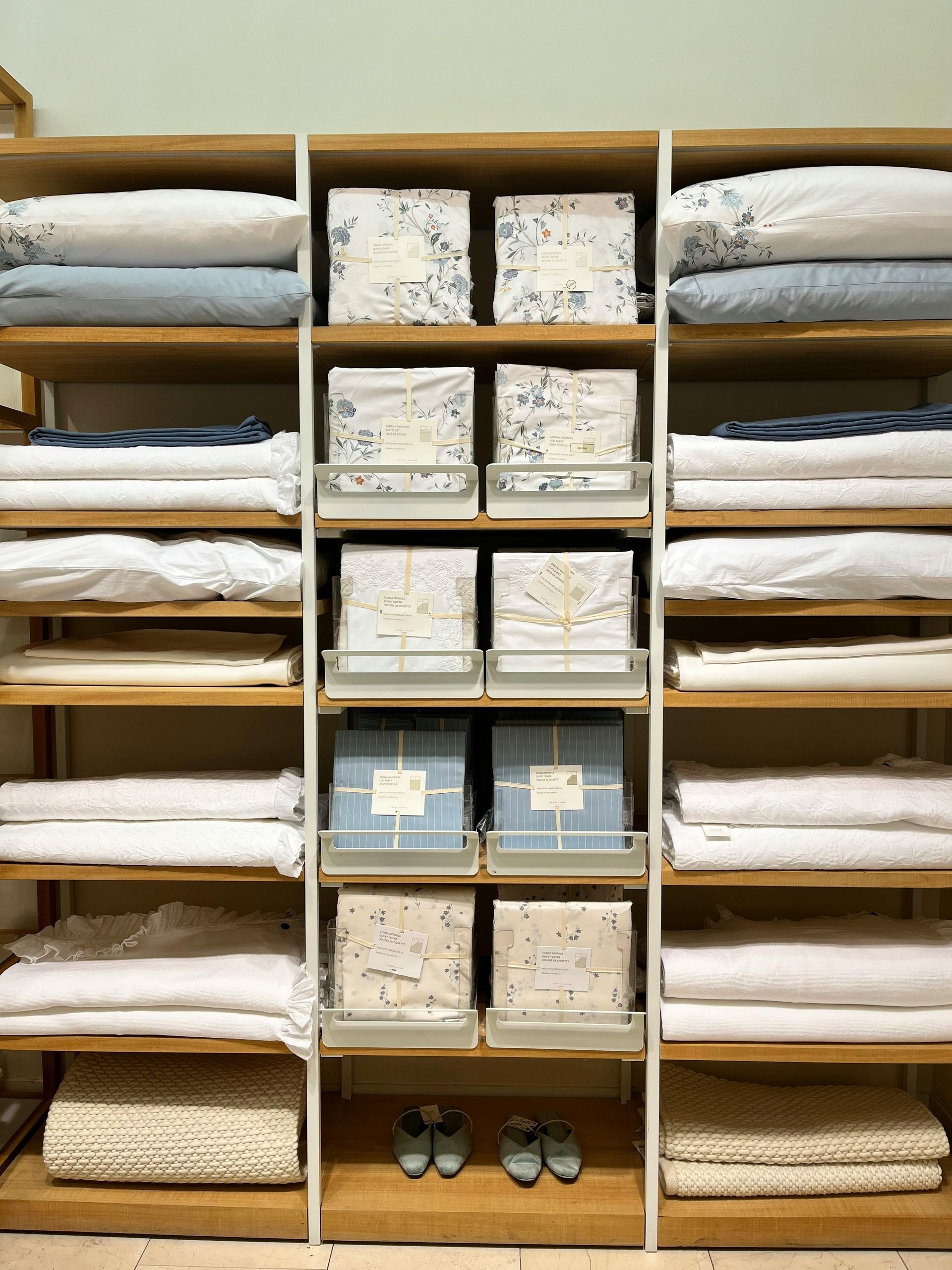 Wooden shelving unit with neatly folded white linens, patterned boxes, and shoes in a storage closet