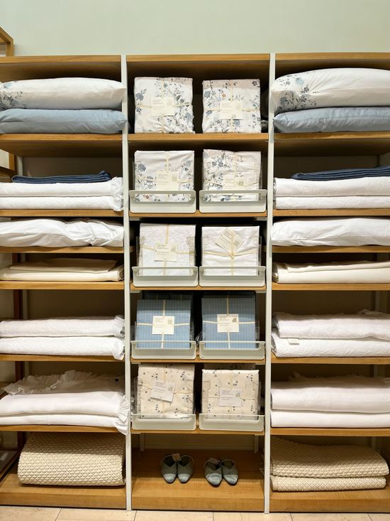 Organized shelving unit with folded bedding, labeled storage boxes, and shoes on the bottom shelf
