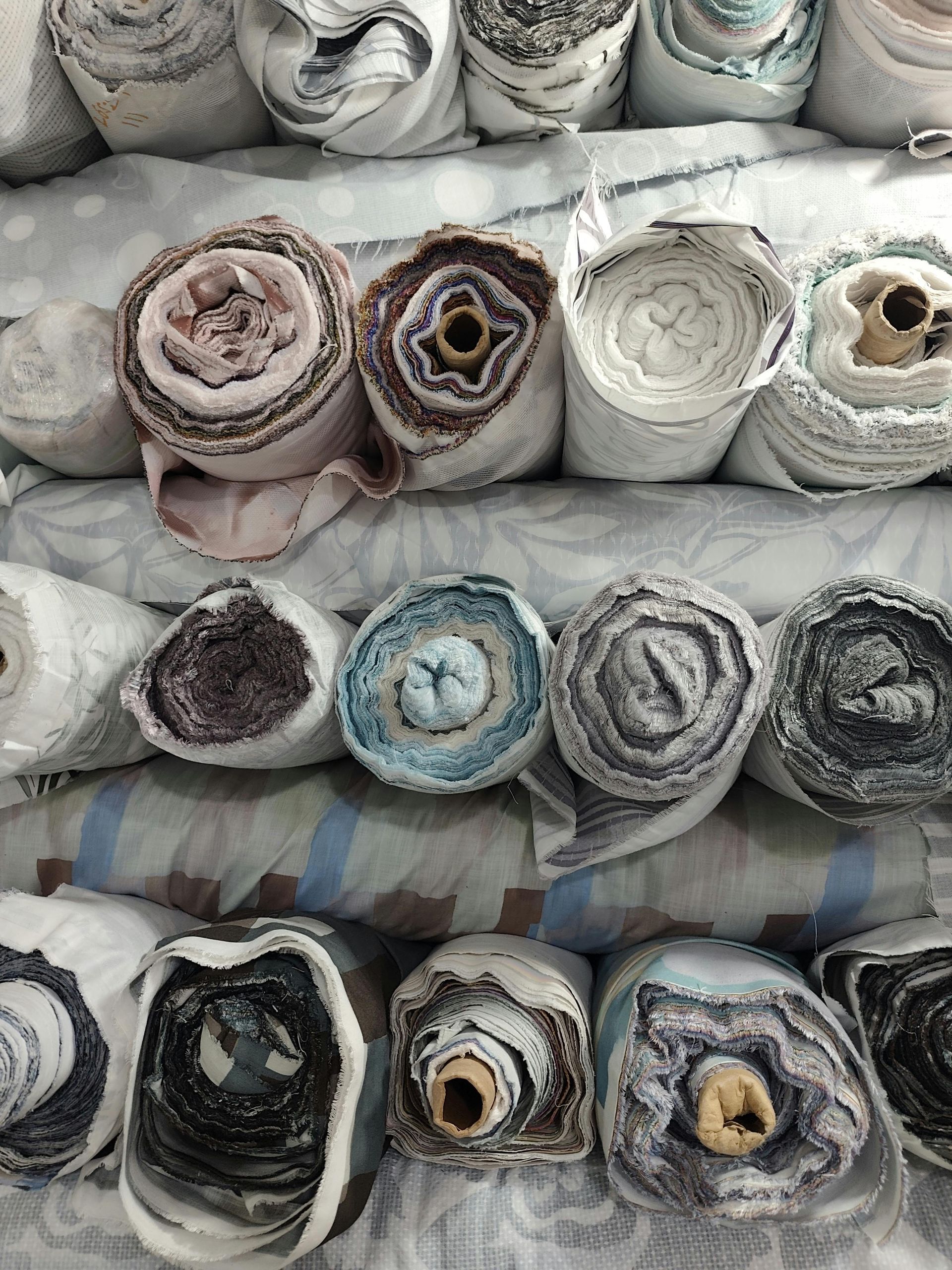 Rolled fabric bundles in muted colors stacked on shelves in a textile shop