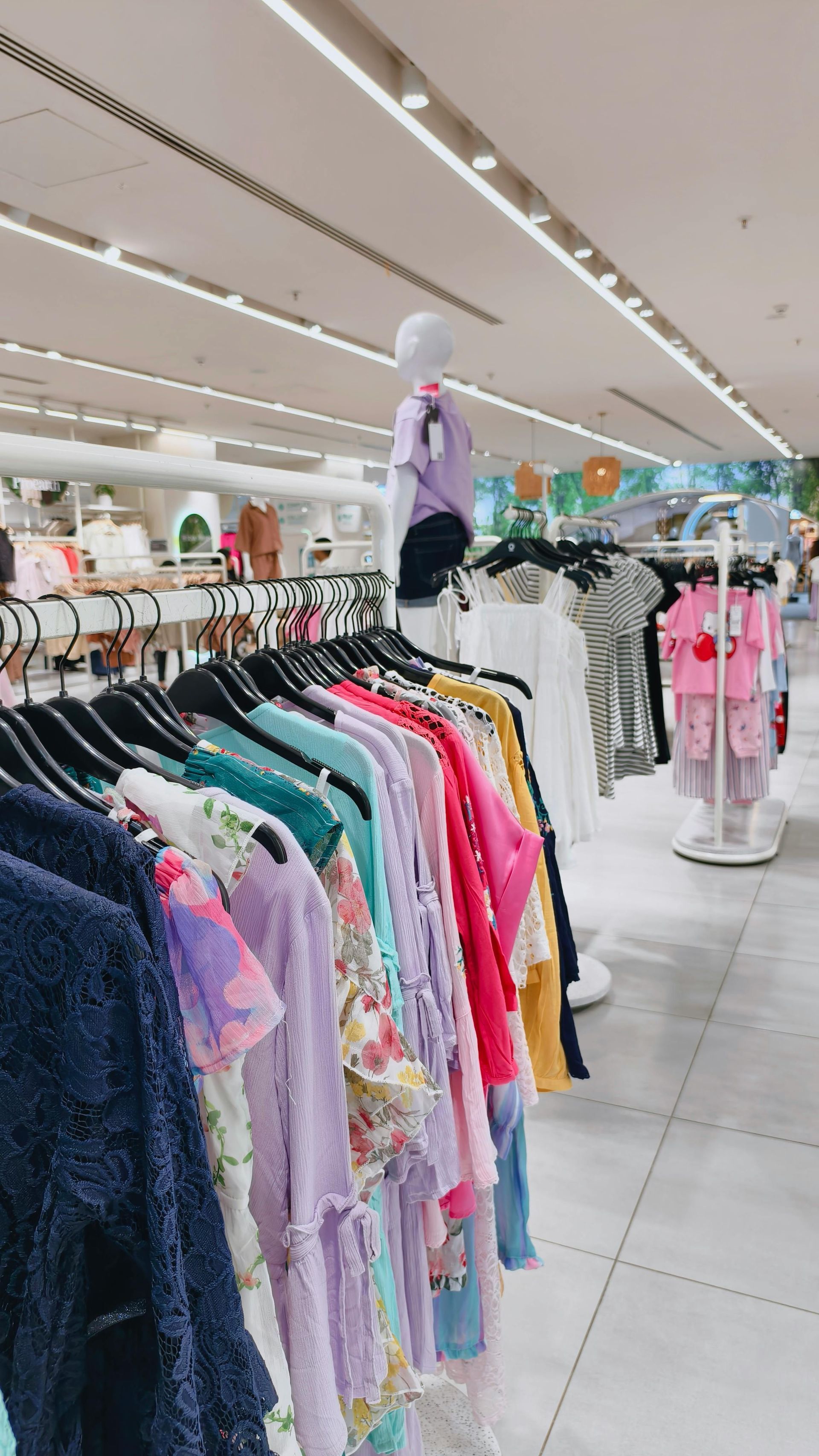 Clothing store aisle with colorful clothes on racks and mannequins under bright ceiling lights
