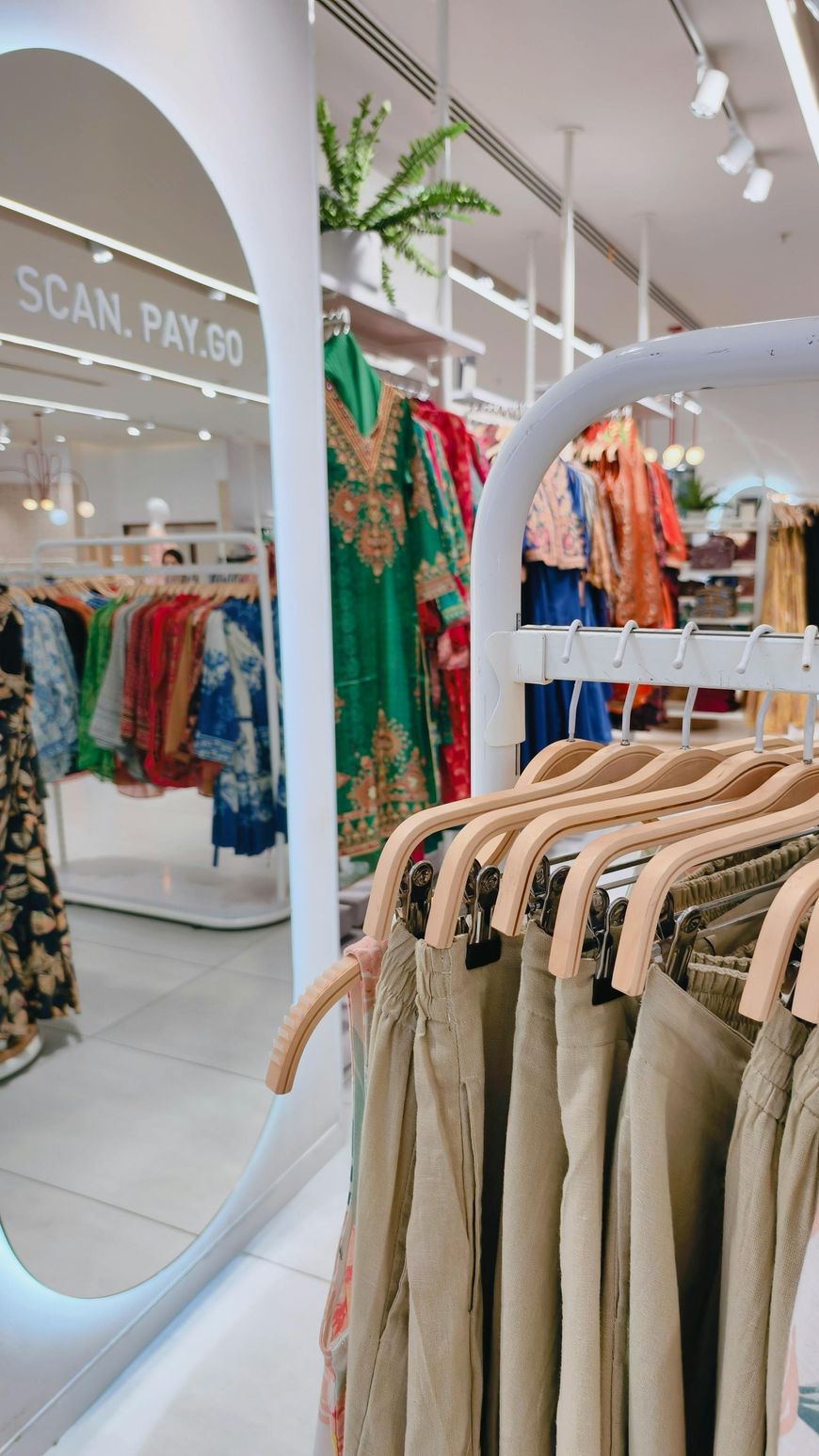 Clothing racks in a bright boutique with a “SCAN, PAY” sign and colorful garments in the background