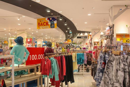 Clothing store interior with sale signs, racks of colorful clothes, and shoppers browsing.