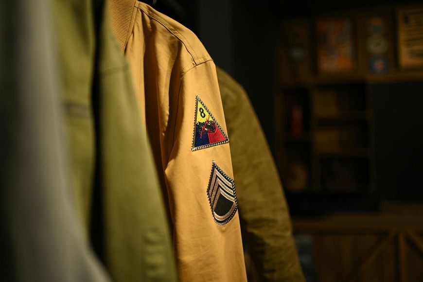 Khaki jacket with scout-style patches hanging indoors, lit by warm sunlight