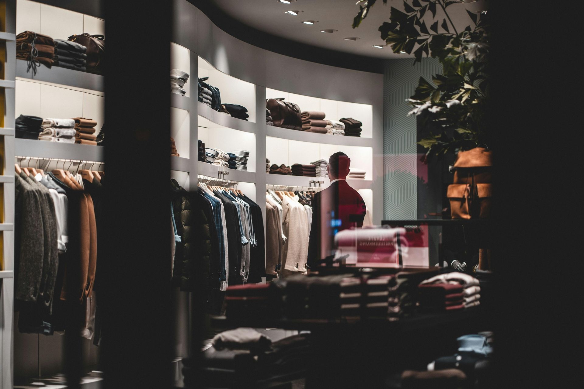Clothing boutique with racks of clothes and a person browsing near a display table