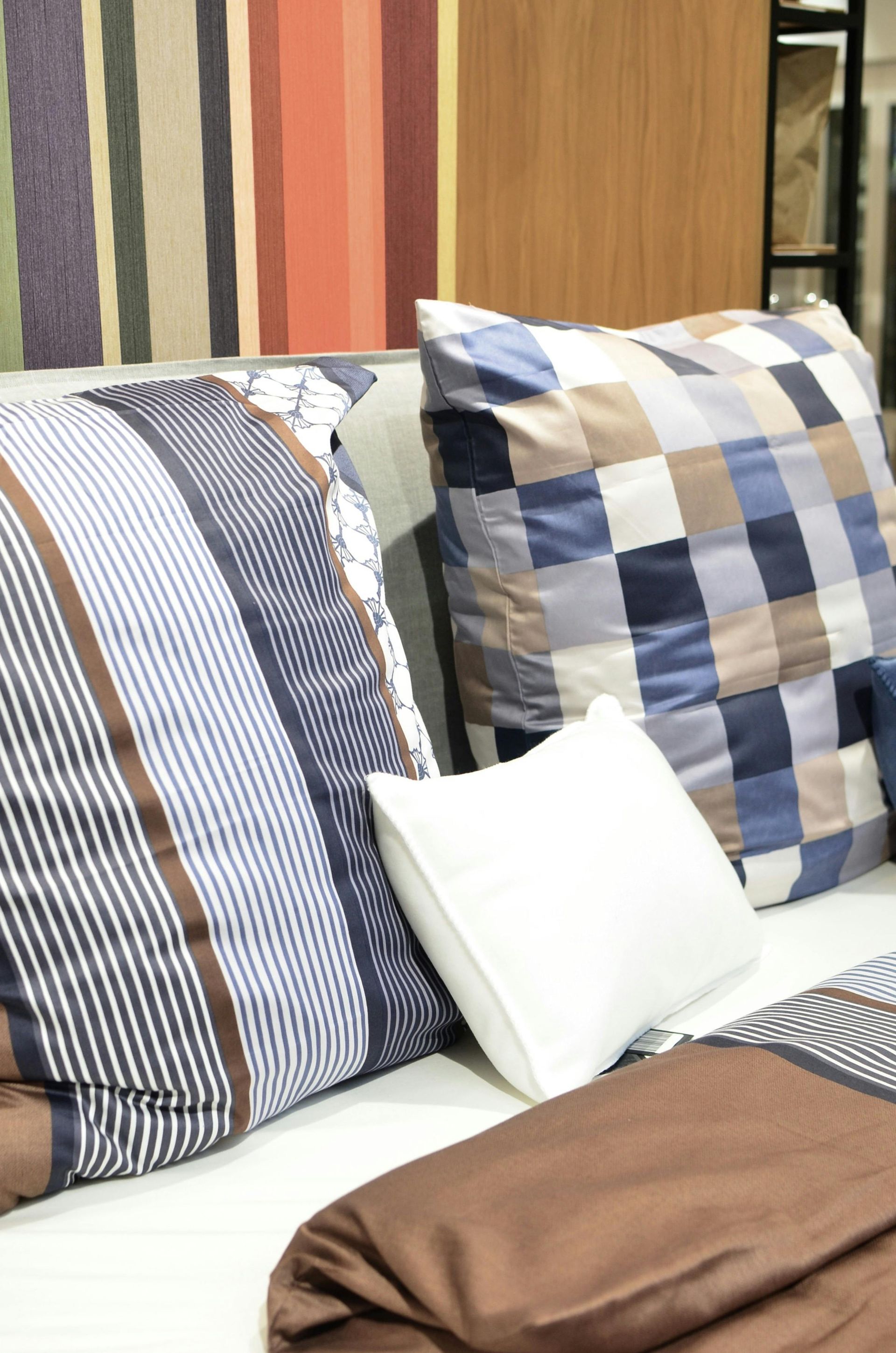 Pillows on a bed with blue, white, and brown plaid covers beside a brown blanket