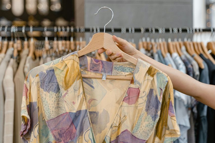Hand holding a colorful patterned blouse on a hanger in a clothing store