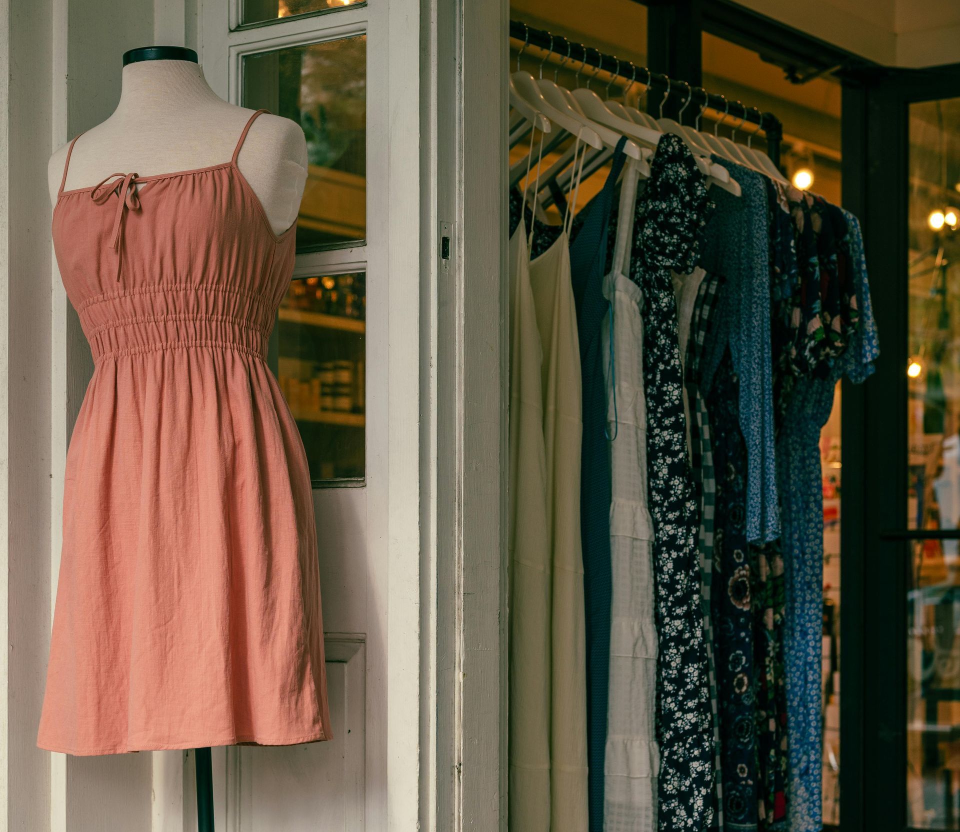 Pink sundress on a mannequin beside a boutique clothing rack with hanging dresses