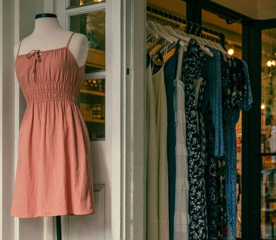 Pink sleeveless dress on a mannequin beside a clothing rack in a boutique