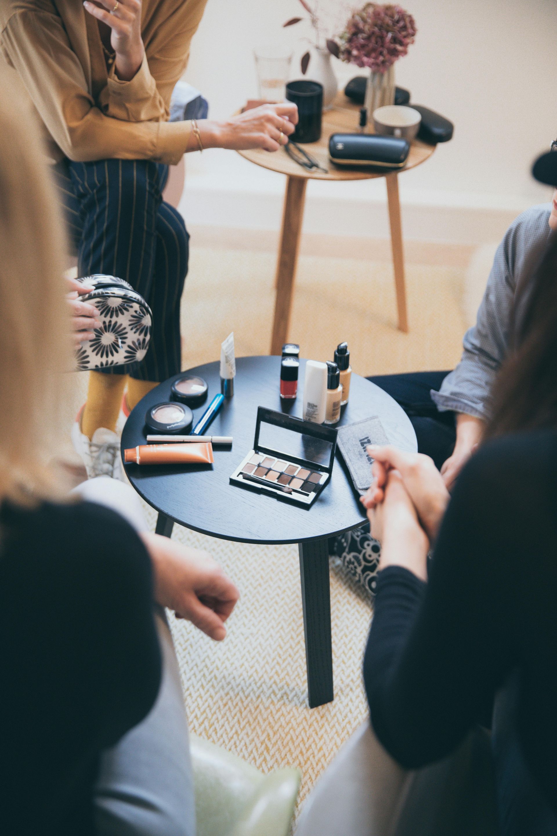 A group of women are sitting around a table with makeup on it.