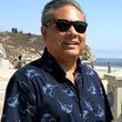 A man wearing sunglasses and a blue shirt is standing on a beach.