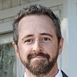 A man with a beard is smiling for the camera while wearing a suit and tie.