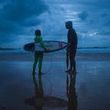 A man and a woman are standing on a beach holding surfboards.