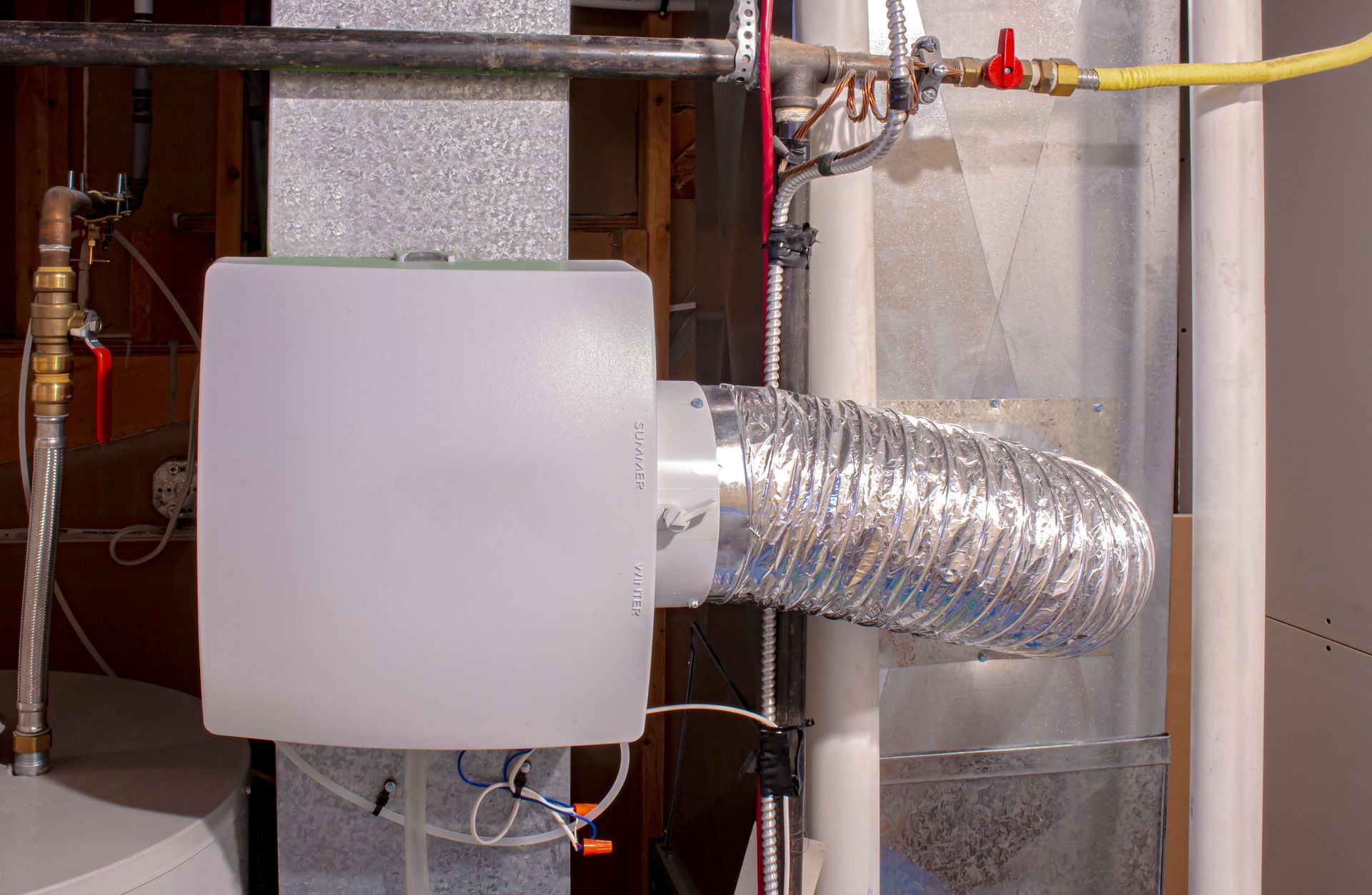 A white box is sitting next to a pipe in a basement.