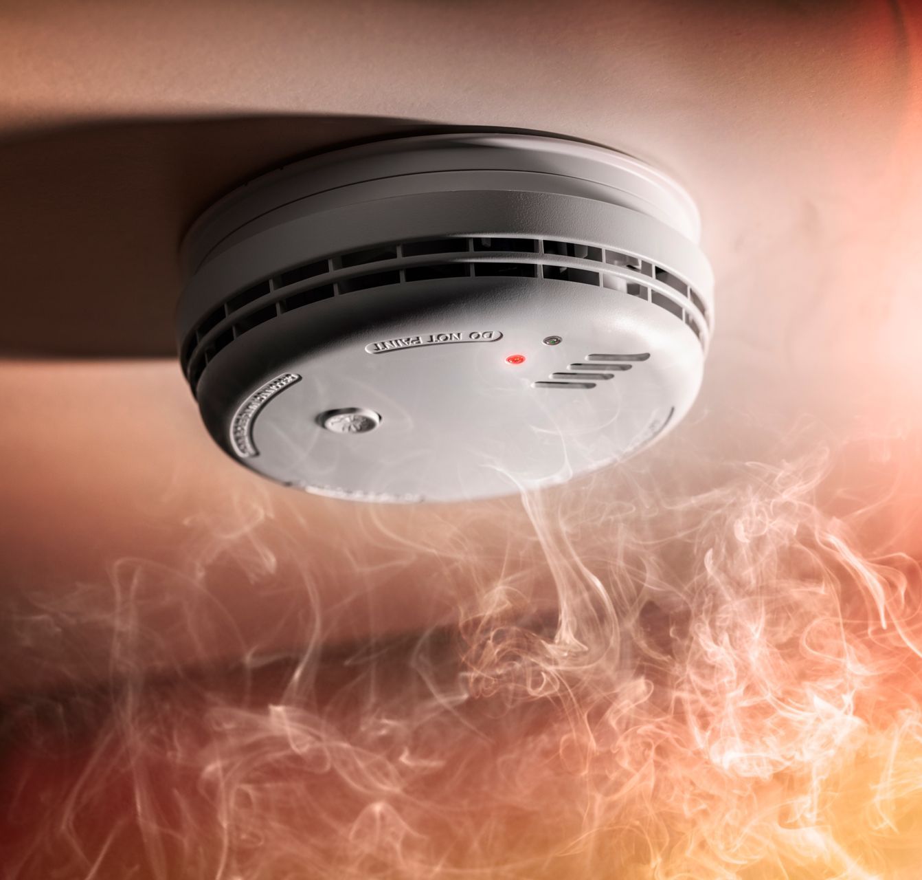 A smoke detector on the ceiling with smoke coming out of it