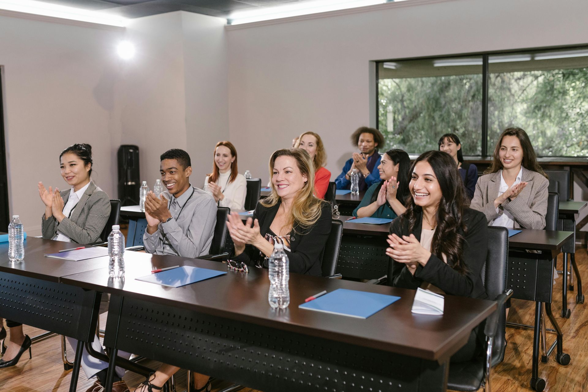 People seated at desks in a classroom, smiling and clapping during a presentation