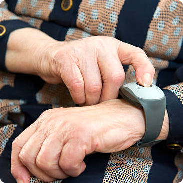 Elderly person's hand pressing a button on a gray medical alert wristband.