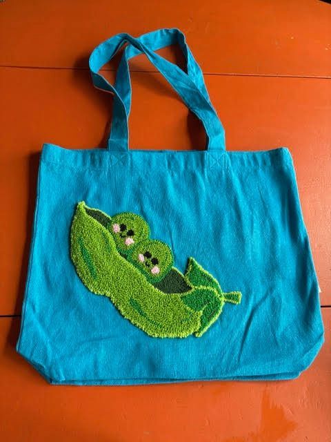 Turquoise draagtas met geborduurde groene erwtenpeul en twee lachende erwten.