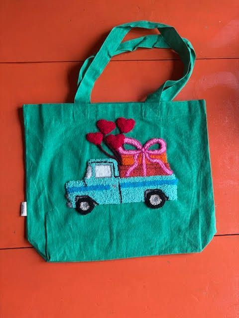 Groene draagtas met een blauwe vrachtwagen die een cadeau en hartvormige ballonnen vervoert.