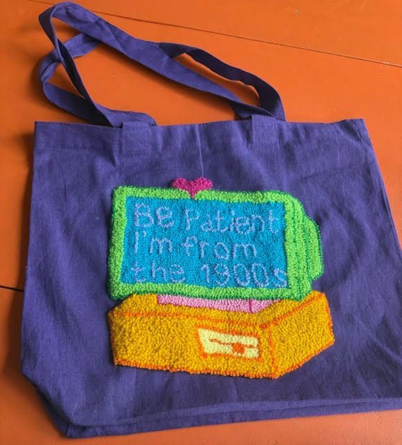 Paarse draagtas met een kleurrijk retro computerontwerp en de tekst 