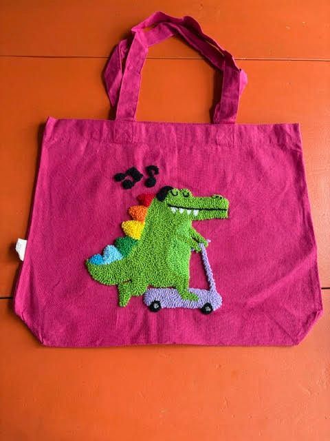 Roze draagtas met een groene dinosaurus op een scooter en muzieknoten erboven.