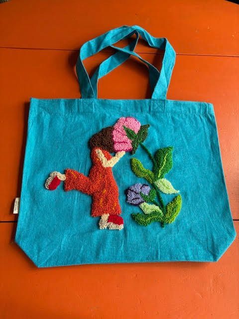 Turquoise draagtas met een geborduurd patroon van een figuur en bloemen, uitgevoerd met de punch-needle techniek.