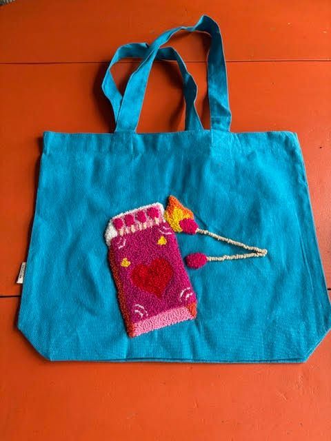 Turquoise draagtas met geborduurd luciferdoosje, inclusief brandende en niet-brandende lucifers; oranje achtergrond.