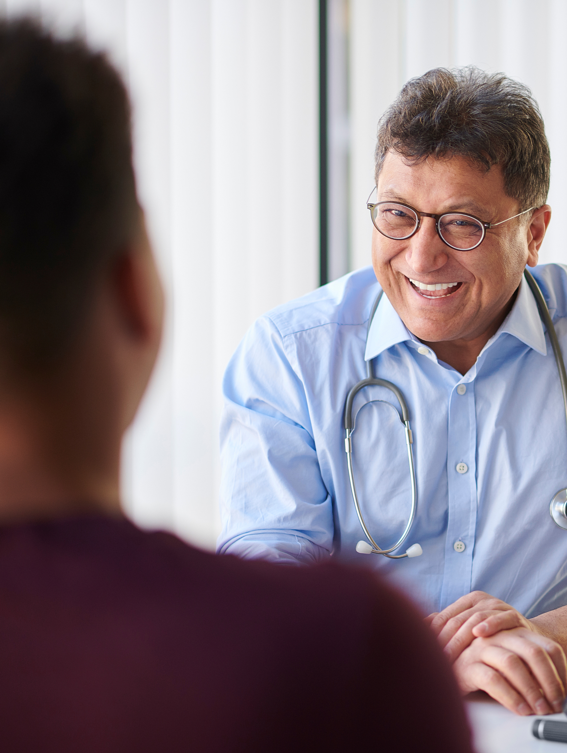 Doctor in blue shirt smiling at patient in office.