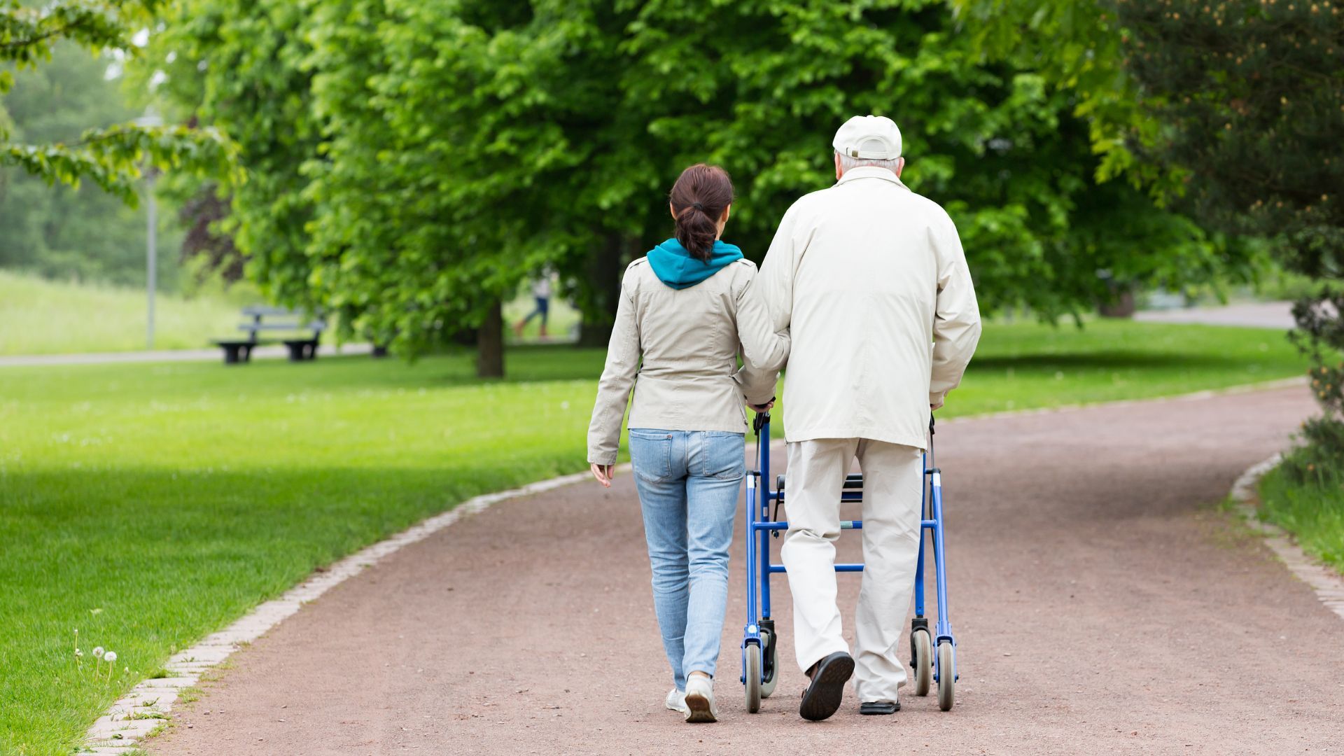Woman assisting an elderly person with a walker on a park path.