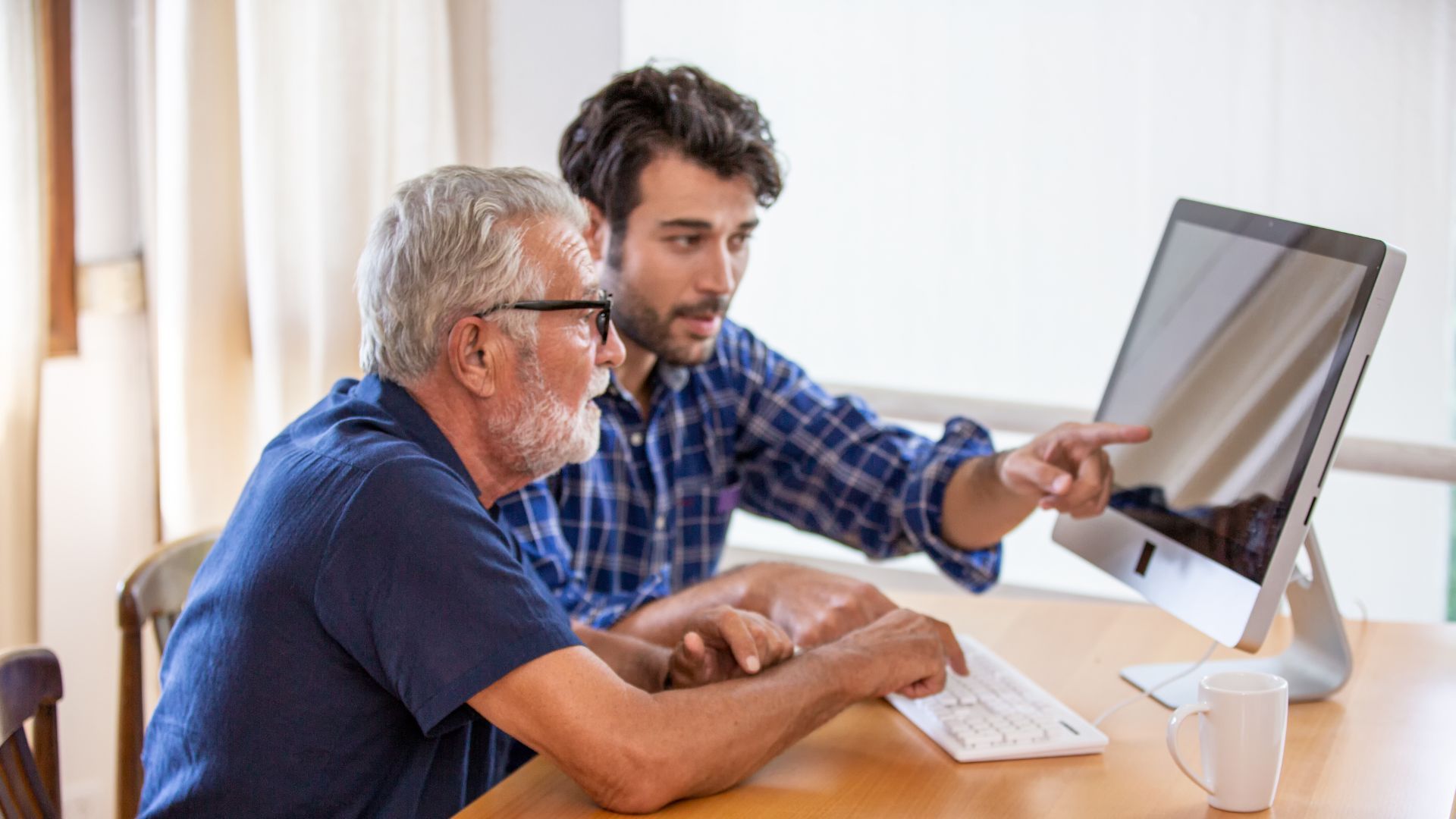 Man assisting older person with computer use; pointing at the screen.