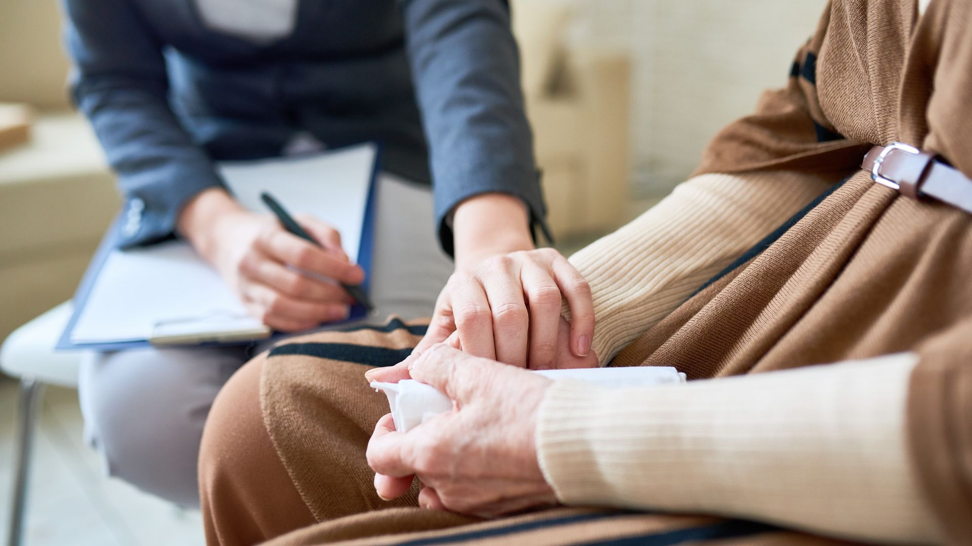 Person holding the hand of another while the other person writes on a clipboard.