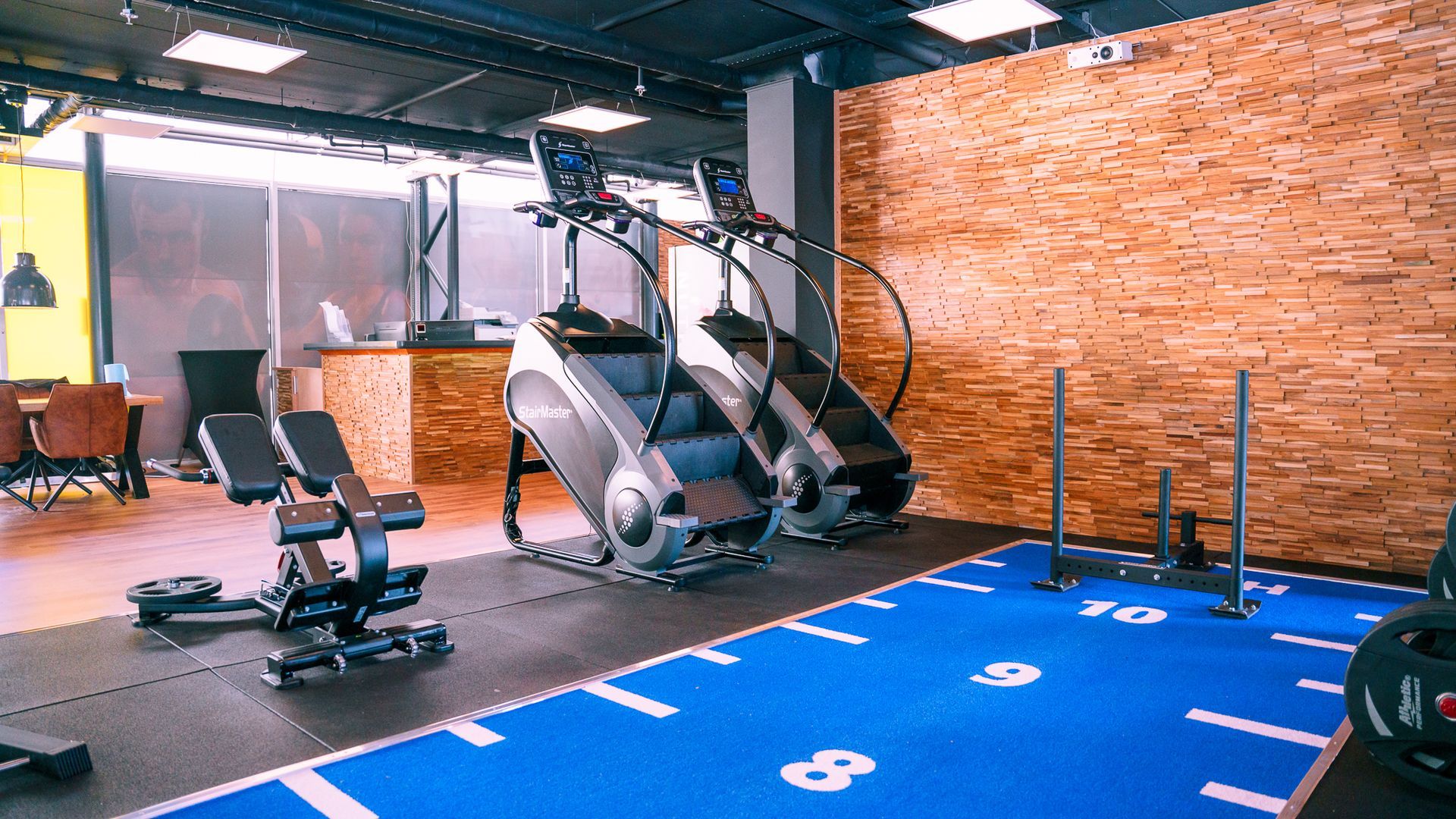 Een sportschool met loopbanden, een bank en een blauwe mat.