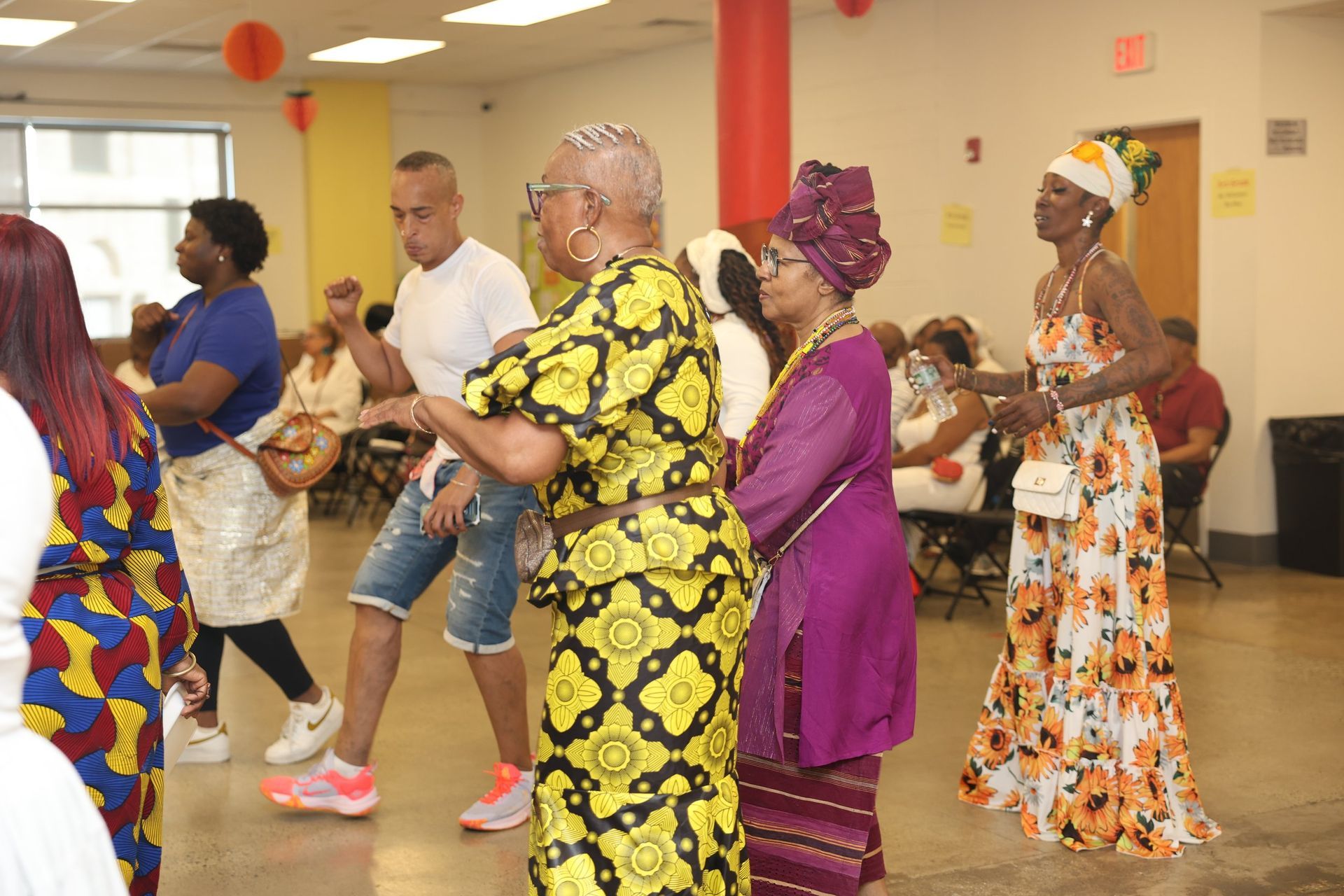 Attendees at a meeting. Woman in red patterned shirt smiles. Others sit at a long table.
