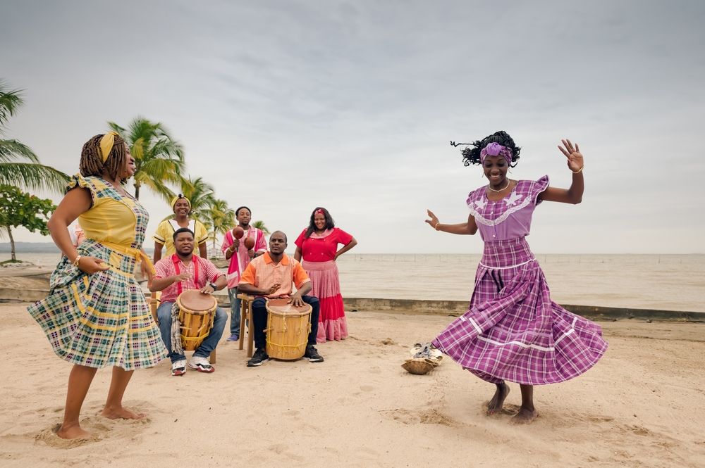 A group of people are playing drums and dancing on the beach.