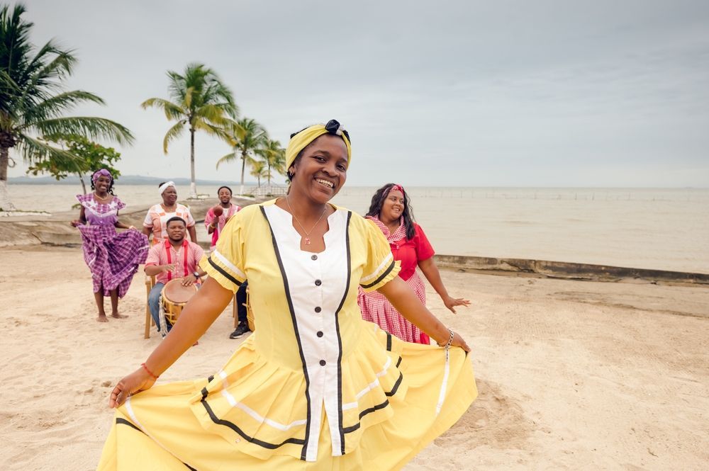 A woman in a yellow dress is dancing on the beach.