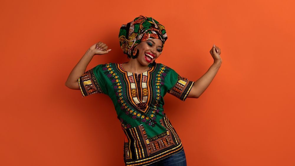 A woman wearing a green shirt and a turban is flexing her muscles.