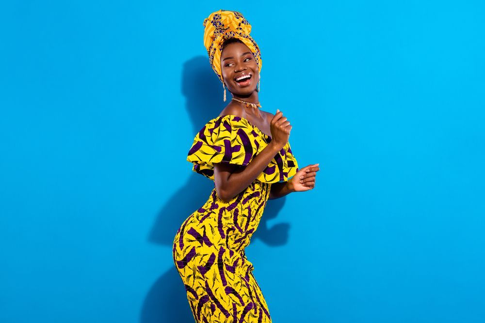 A woman in a yellow dress and head scarf is dancing on a blue background.