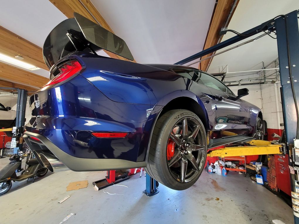 Blue Ford Mustang on a lift in a garage, featuring a large spoiler and red brake calipers.