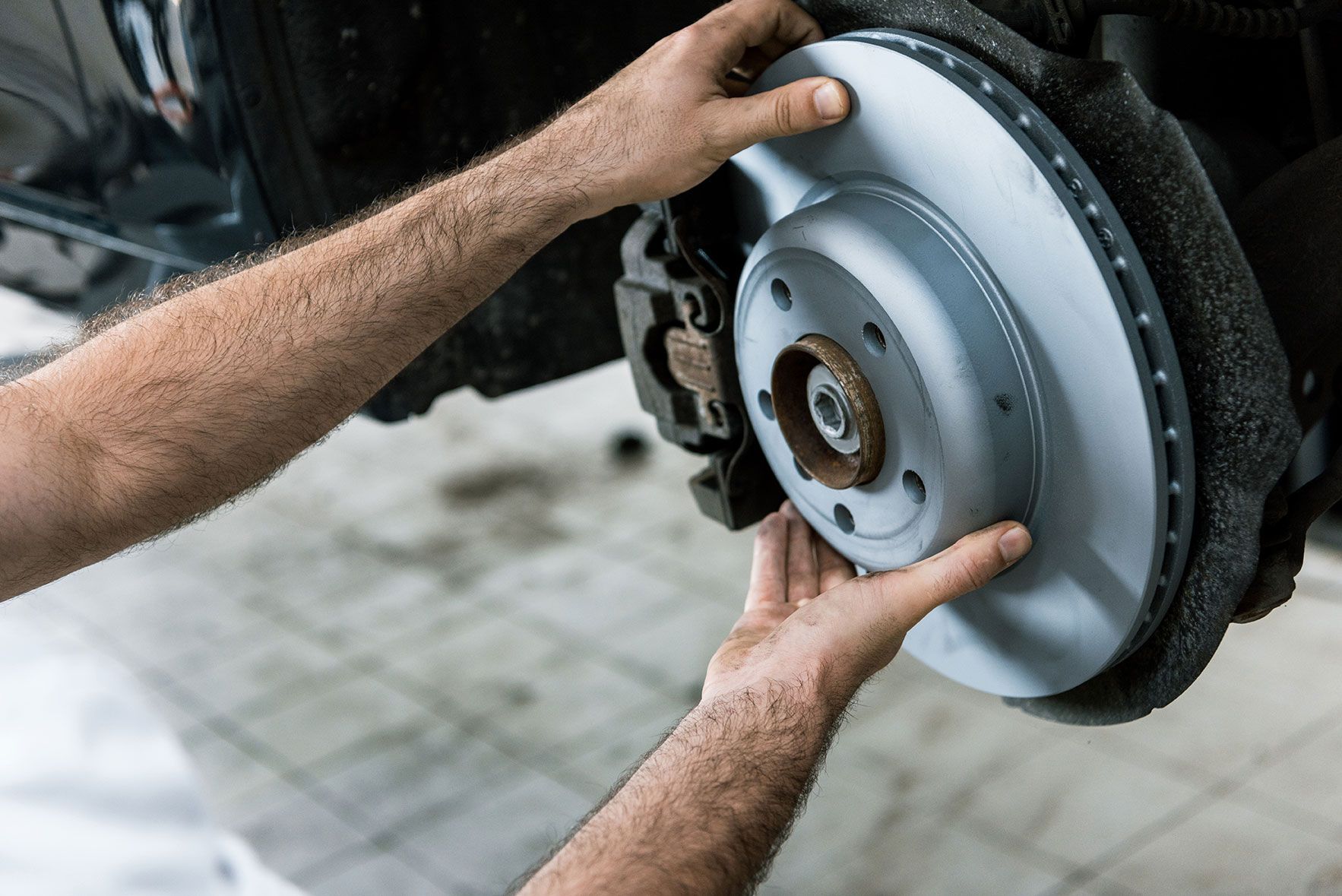 Hands installing a new car brake rotor on a vehicle in a garage setting.