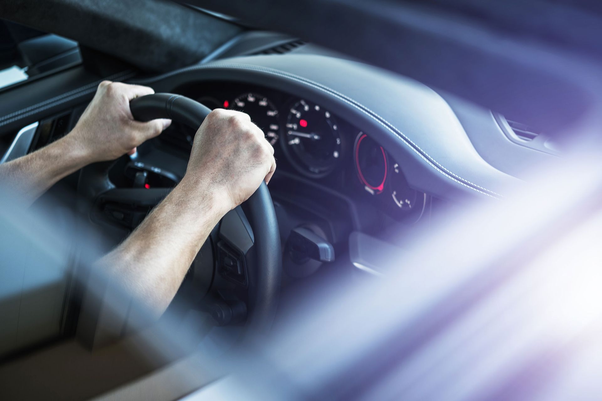 Hands gripping a car steering wheel; dashboard and front window visible.