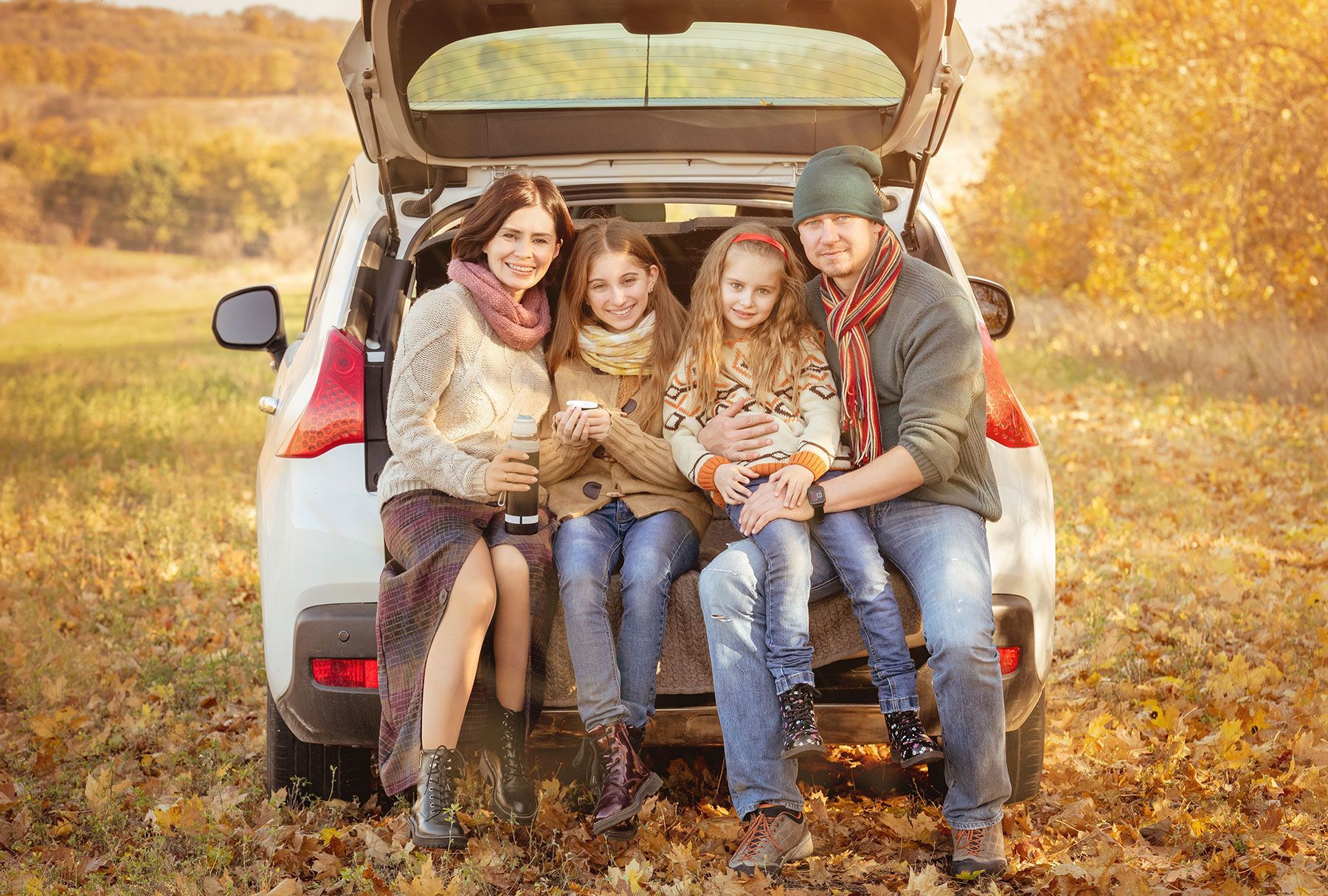 Family sitting in car trunk in a field; smiling, fall colors.