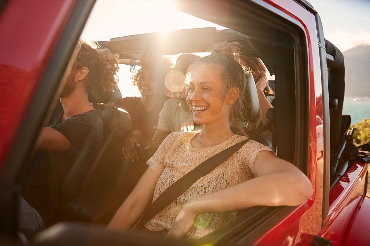 People in a red car, smiling, driving with the sun shining through.