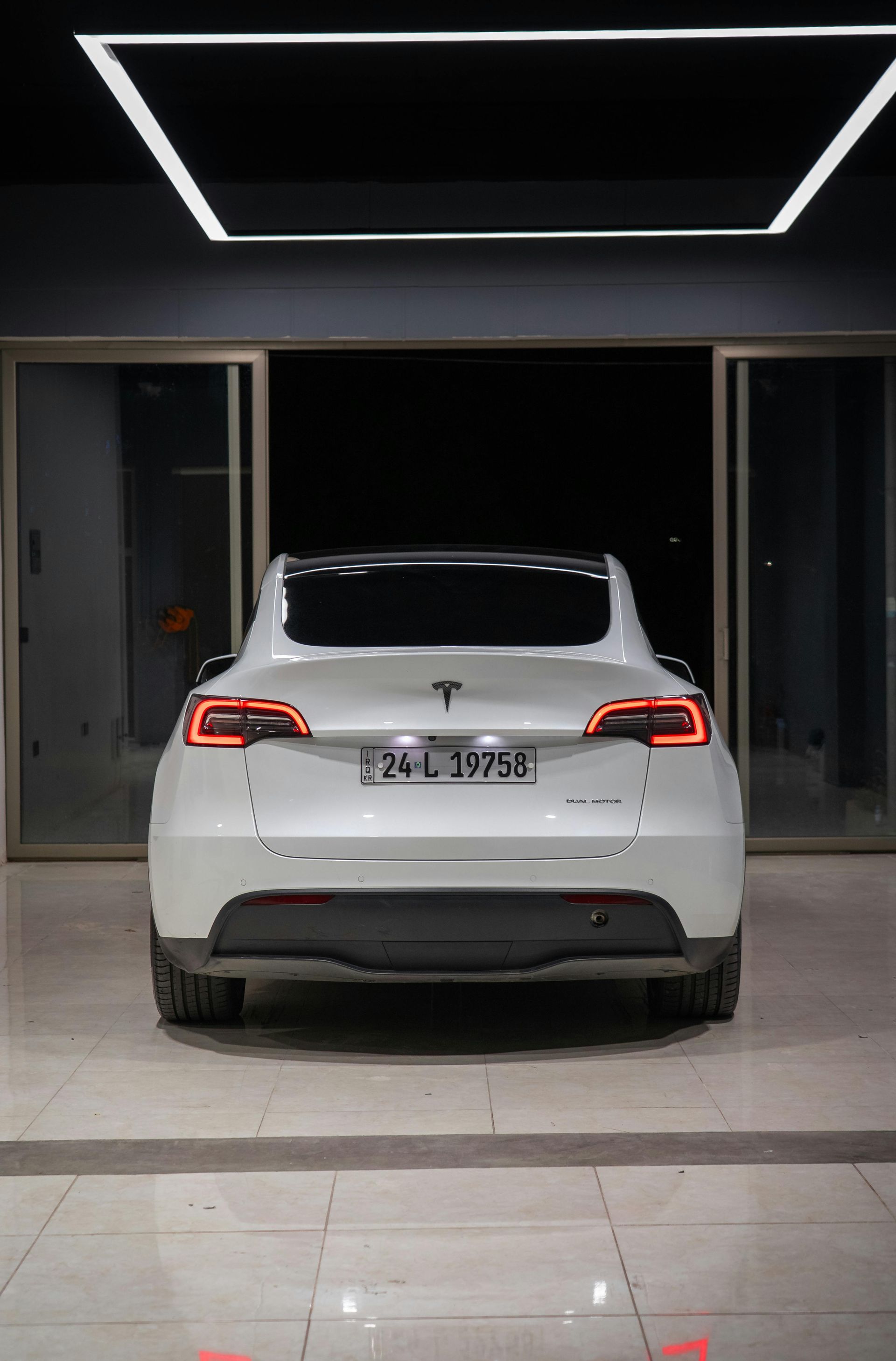 White Tesla SUV parked in front of glass doors, under a bright light.