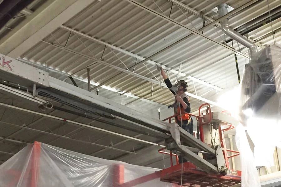 Une personne dans une cabine de ascenseur, portant un harnais de sécurité et un masque, vaporise de la peinture blanche sur un plafond