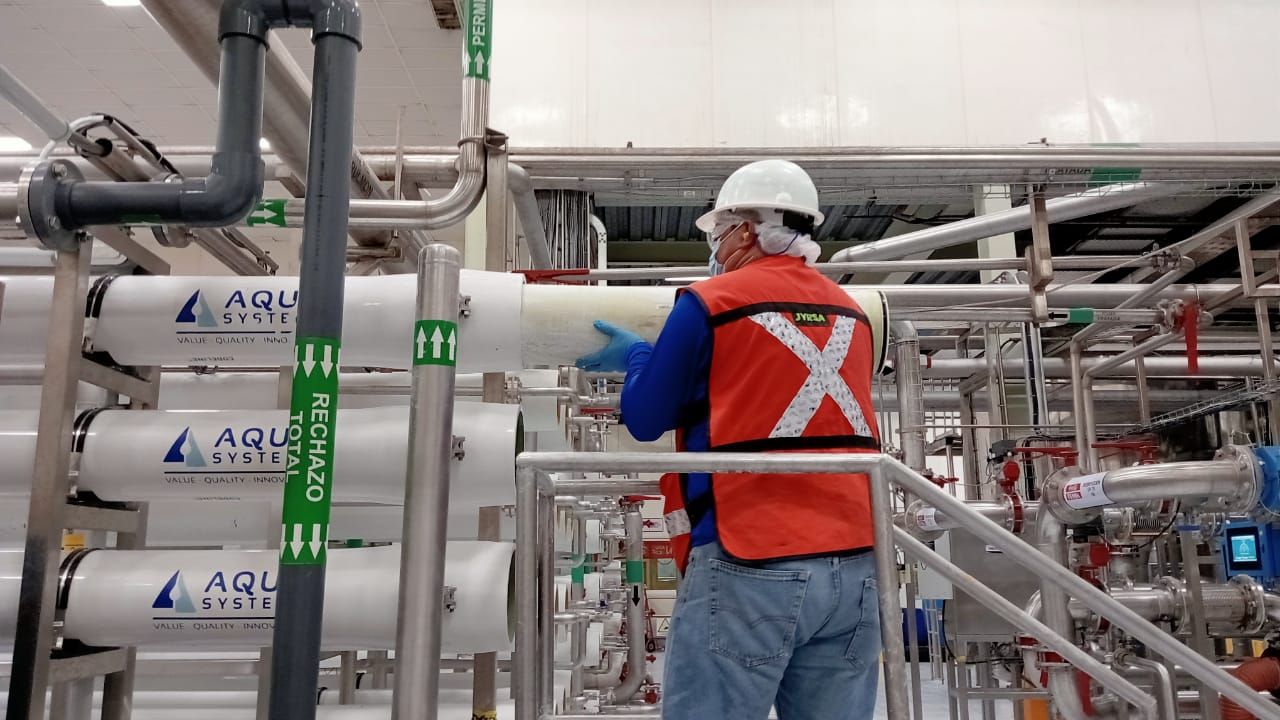 Persona con chaleco de seguridad examina el equipo de purificación de agua en un entorno industrial.