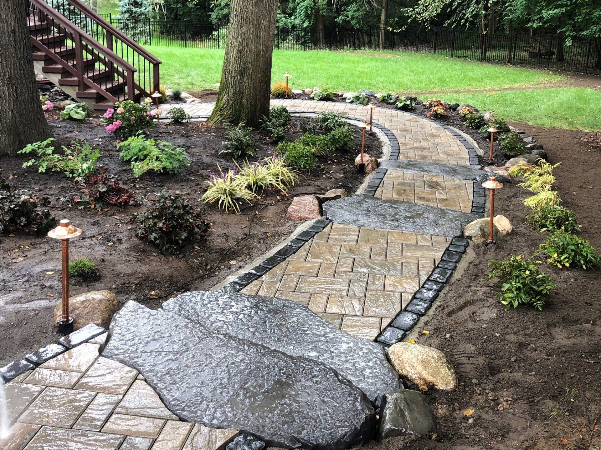 Stone pathway winds through a garden with plantings and small lights.