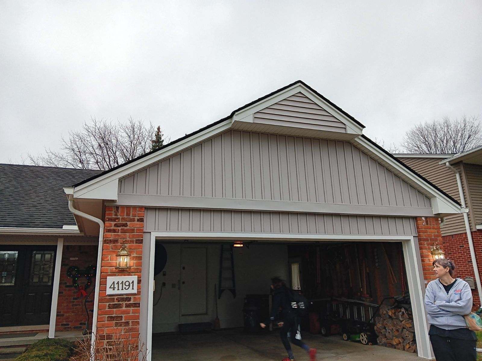 Garage exterior with person; brick, tan siding, cloudy sky.